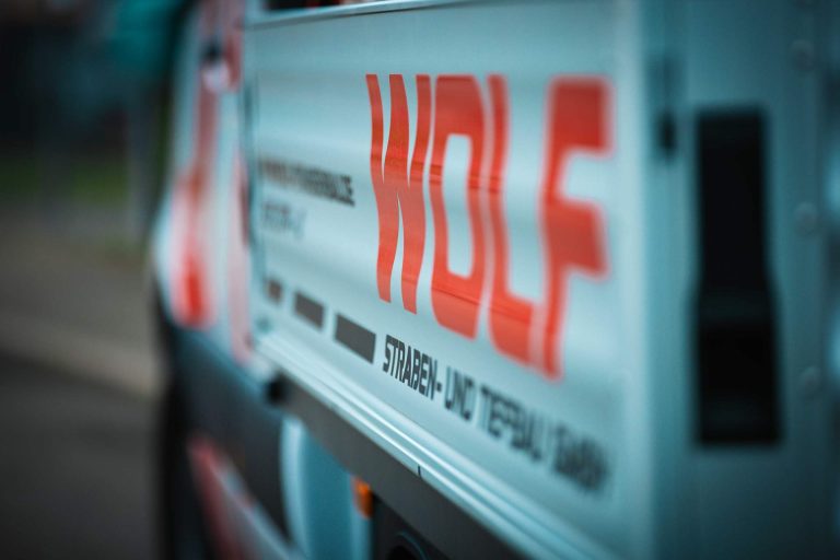 Nahaufnahme eines WOLF Firmen-Logos in Rot und Weiß auf der Plane oder Seite eines Baufahrzeugs.