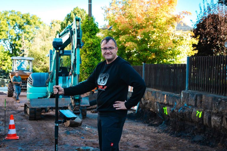 Nicky Dohms lächelt auf der Baustelle, in der Hand ein Roverstab. Er repräsentiert das qualifizierte Team von Wolf.