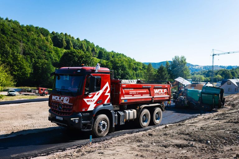Roter WOLF Kipplaster auf einer Straßenbaustelle bei Asphaltierungsarbeiten im Grünen.