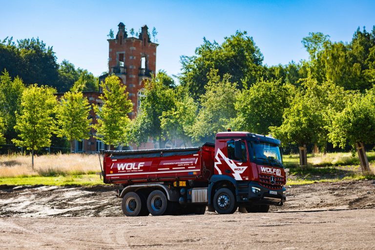 Lastwagen der Firma WOLF im Erdbau bei Bauarbeiten vor einer historischen Ruine oder einem Schloss.
