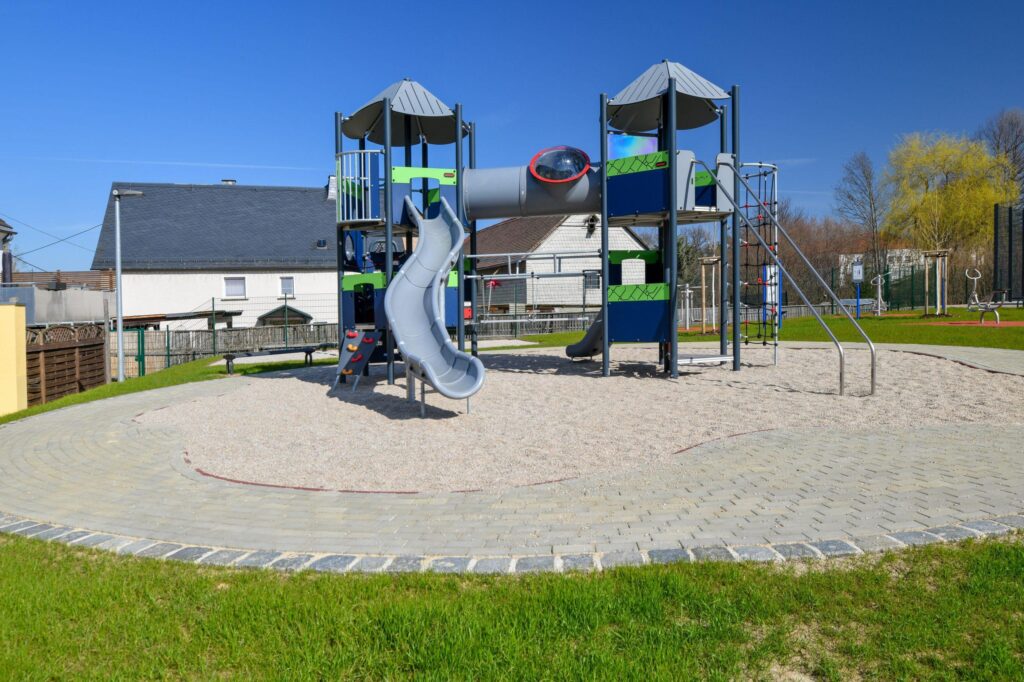 Neuer Spielplatz mit Sandfläche, Spielturm, Rutsche und Schaukeln.