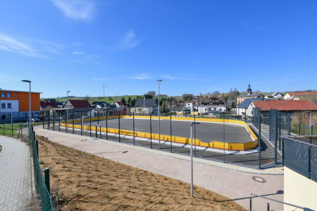 Neuer, fertiggestellter Sport- oder Spielplatz mit gelben Banden und Zaun.