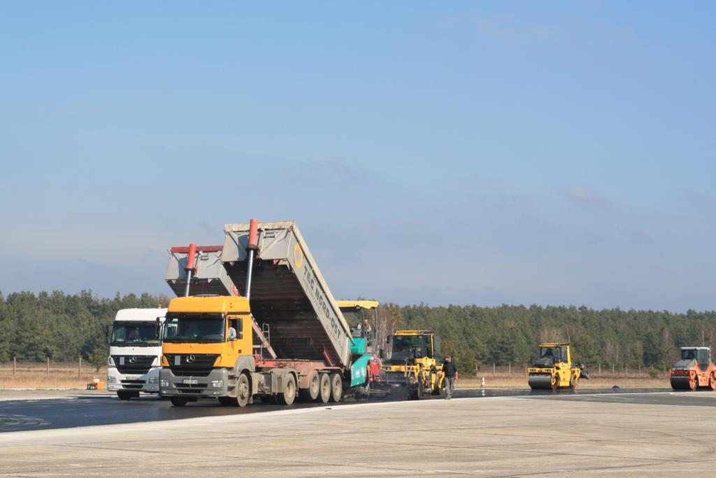 Hier ist der Kern des Asphaltstraßenbaus zu sehen: Ein schwerer Muldenkipper entlädt das heiße Asphaltmischgut in den Asphaltfertiger. 