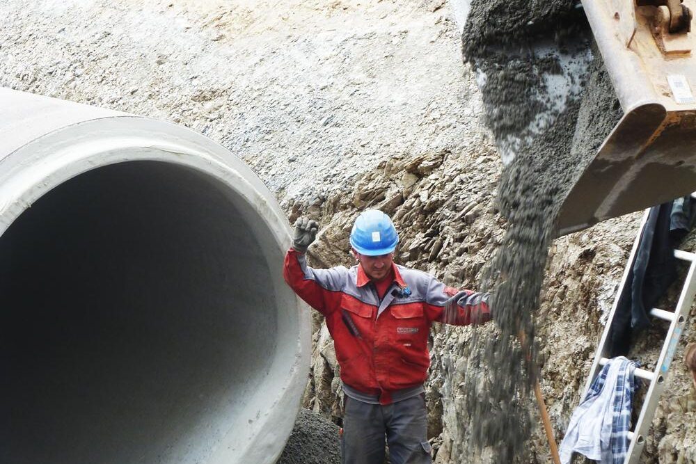 Arbeiter mit Helm und Schutzkleidung inspiziert ein großes Betonrohr im Schacht.