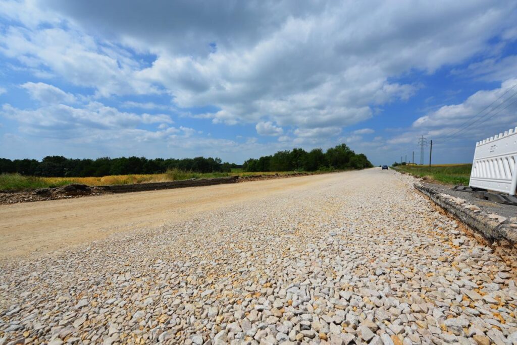 Blick über eine lange, vorbereitete Schottertragschicht (Kies/Recyclingmaterial).