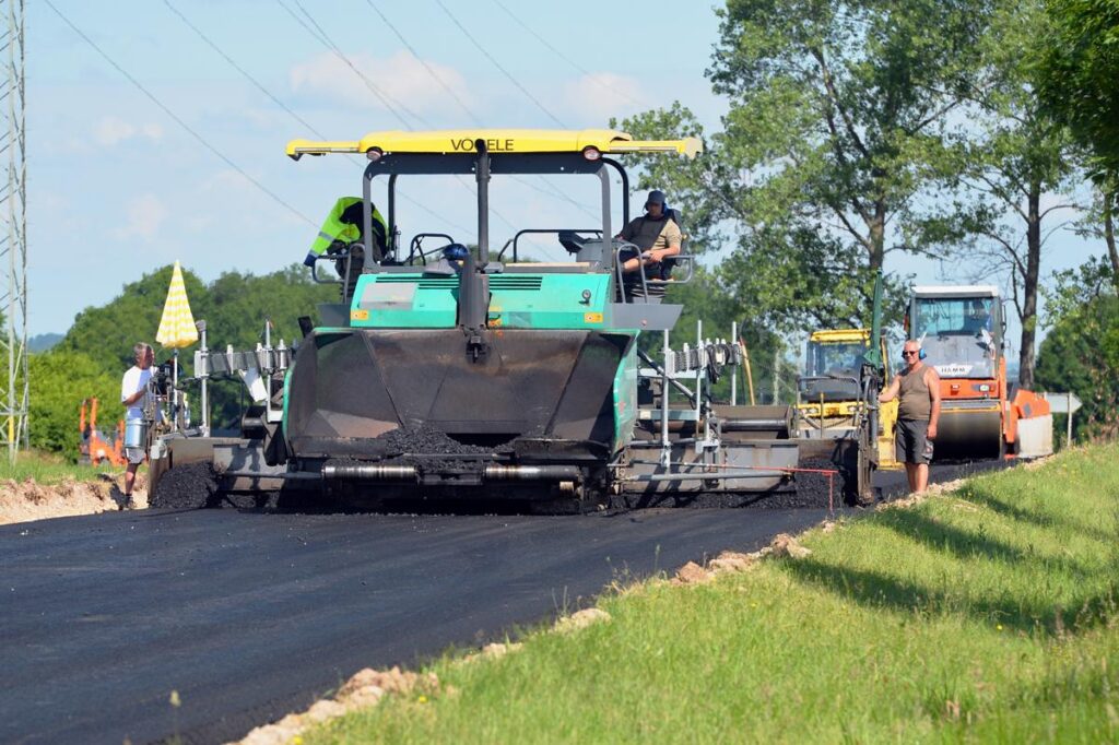 Asphaltfertiger baut die Binderschicht oder Deckschicht ein, Walzen folgen im Hintergrund.