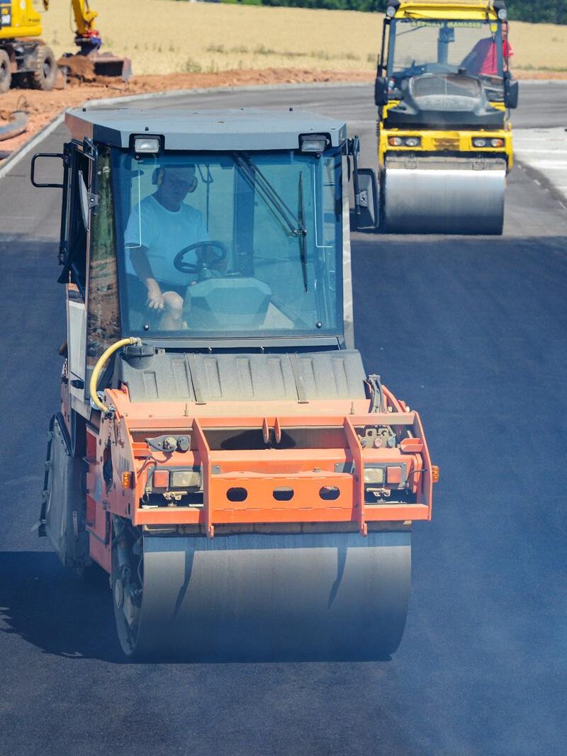 Tandemwalze verdichtet die neue Asphaltfläche auf der Baustelle, Fokus auf den Fahrer bei der Arbeit.