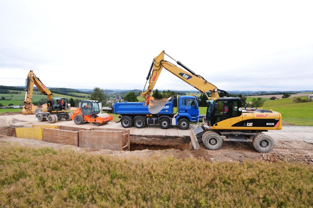 Bagger und Muldenkipper beim Erdaushub für einen breiten Graben in ländlicher Umgebung.