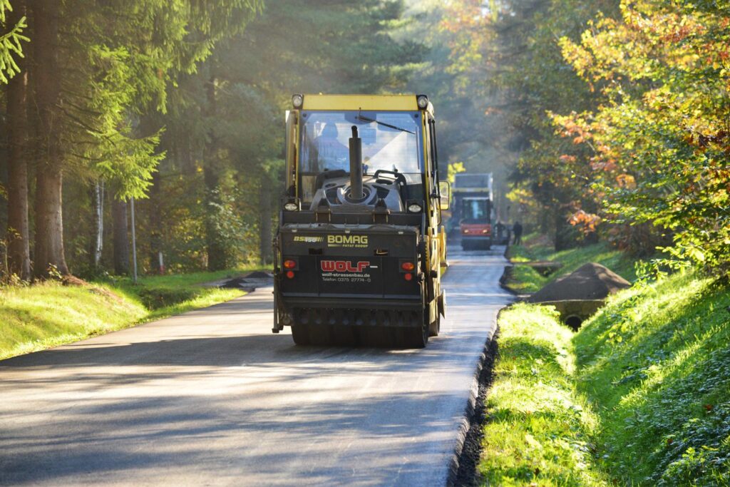 Walze verdichtet den Randstreifen der neuen Asphaltstraße; altes Material liegt rechts.