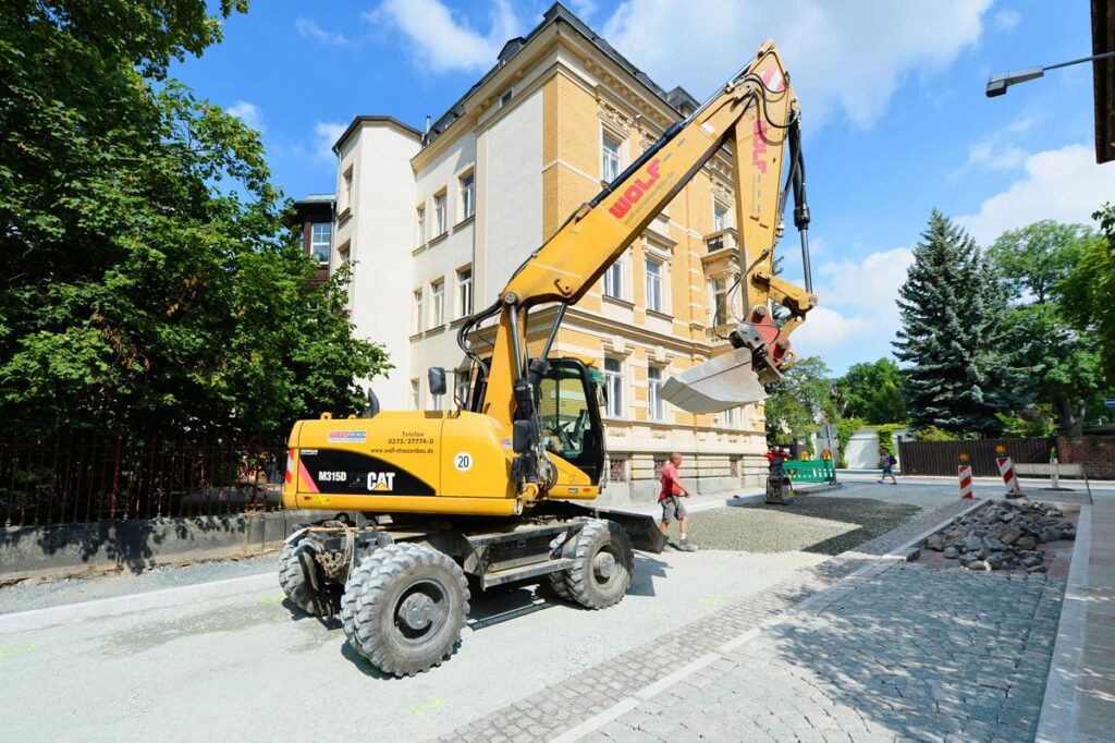Gelber Mobilbagger auf einer gepflasterten Straße vor einem Altbau in Reichenbach.