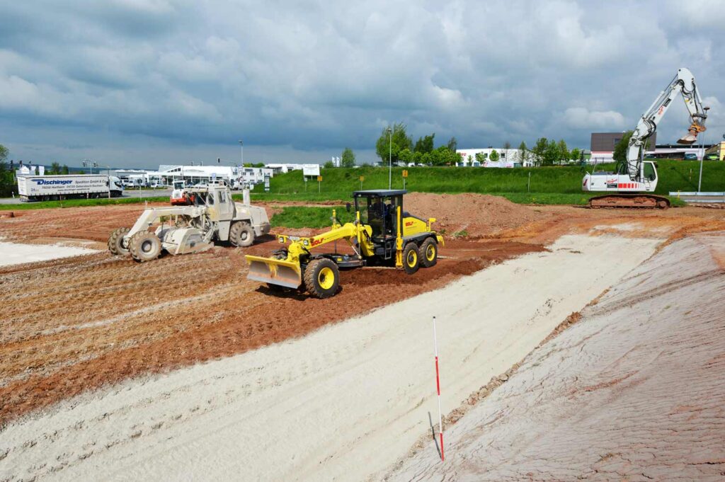Erdarbeiten und Feinplanierung der Parkfläche durch Grader und Radlader auf der Sachsenring-Baustelle.
