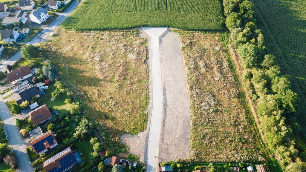 Luftaufnahme eines T-förmigen, Weges, umgeben von Feld und Einfamilienhäusern der Wohnsiedlung