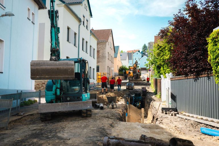 Kleiner Minibagger der Firma Wolf im Einsatz beim Aufbrechen von Straßenbelag für Tiefbauarbeiten.