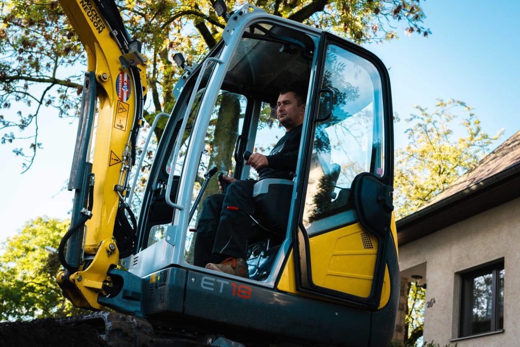 Nahaufnahme eines Bauarbeiters in der Kabine eines Wacker Neuson ET18 Minibaggers, der die Bedienelemente auf einer Baustelle steuert.