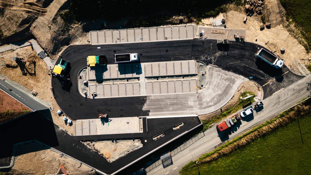 Luftaufnahme einer Parkplatz-Baustelle mit einer Kombination aus gepflasterten Stellflächen und frisch asphaltierten Fahrwegen.