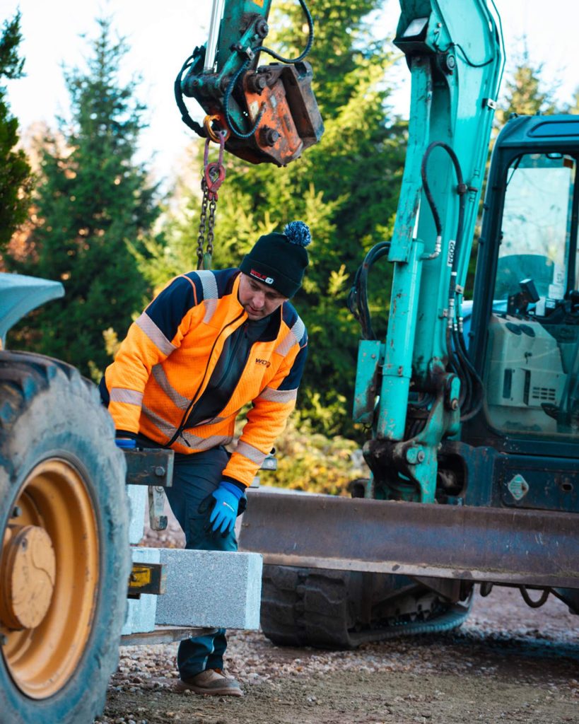 Präzise Handarbeit im Straßenbau: Ein Mitarbeiter setzt Granit-Bordsteine in ein Betonbett. Diese Naturstein-Details sorgen für eine hochwertige Optik und Langlebigkeit der neuen Infrastruktur in Wildenfels.