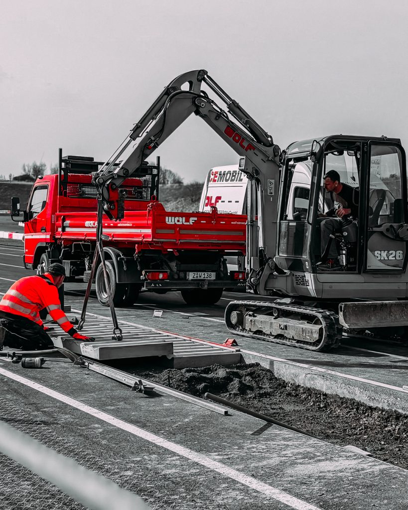 Bauarbeiten an der Rennstrecke: Wolf-Mitarbeiter und Minibagger bei der Installation von Curbs und Streckenelementen.